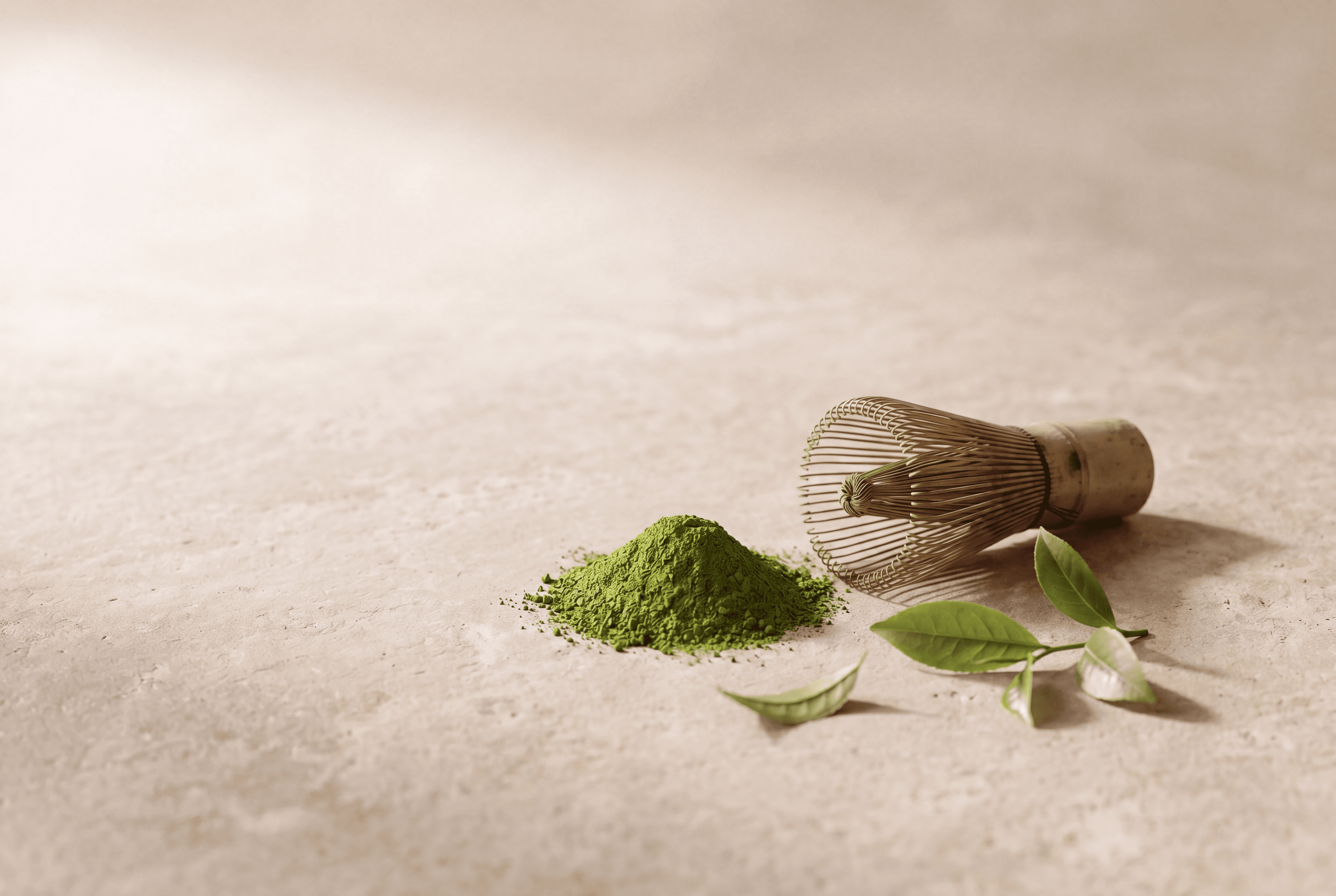 Matcha powder, a bamboo whisk, and tea leaves on stone